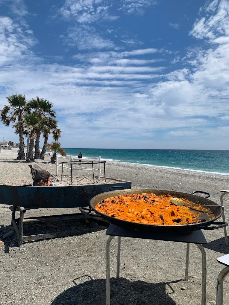 Paellera de arroz junto a la barca de los espetos, frente al mar y las palmeras