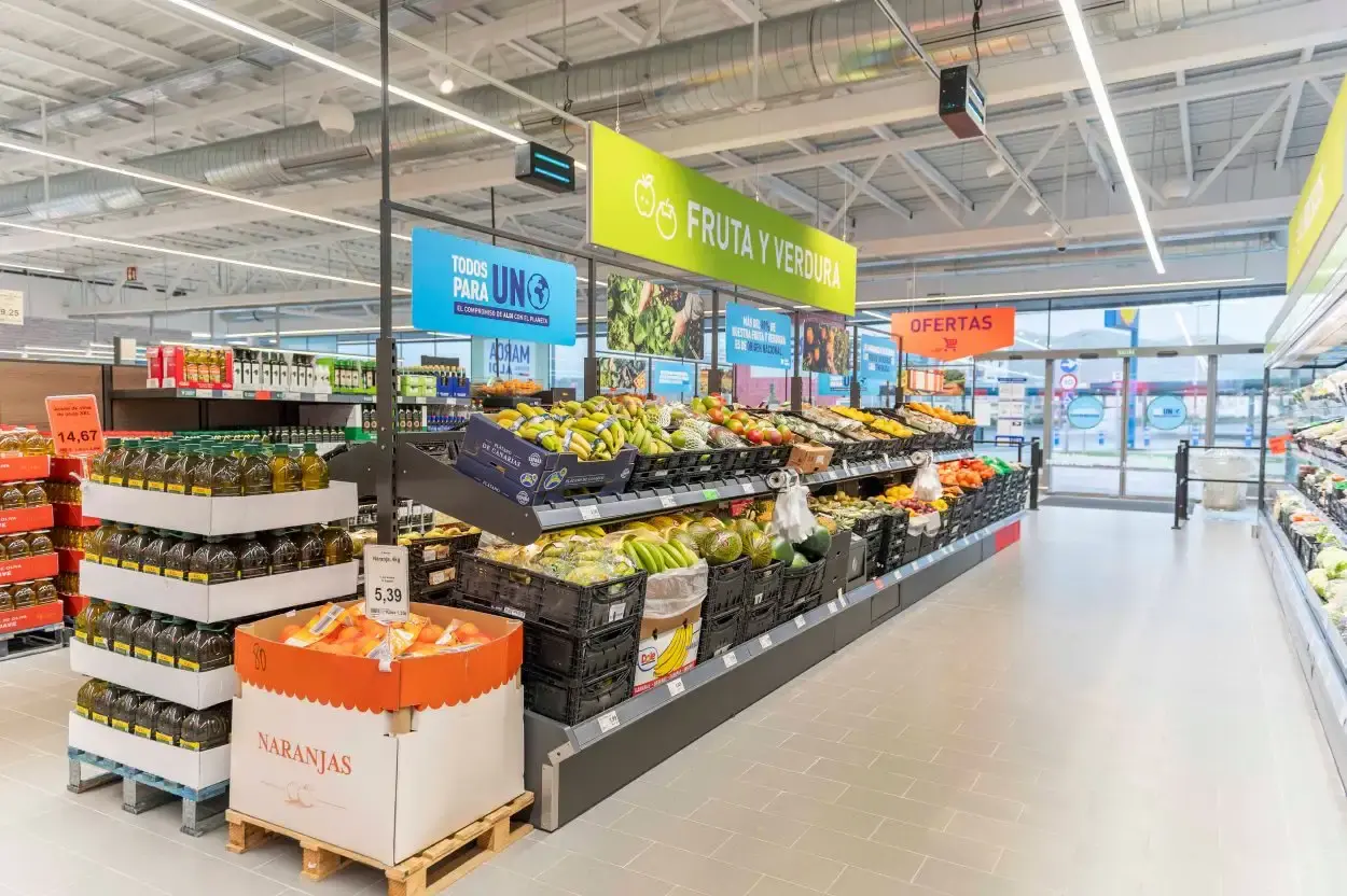 Sección de fruta y verdura con cajas de naranjas y ofertas a la entrada del supermercado