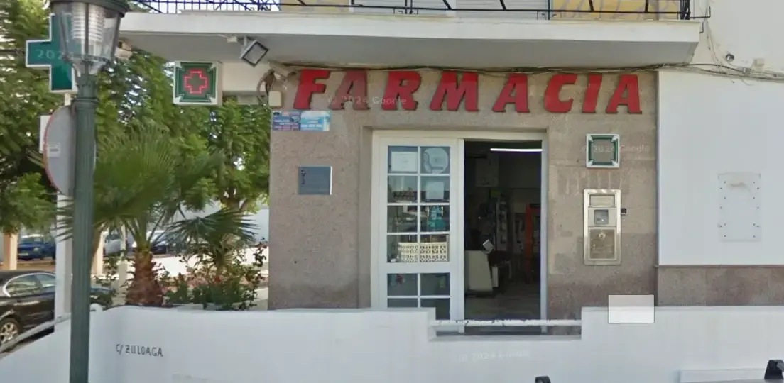 Fachada de la farmacia junto al ambulatorio, con rótulo rojo de Farmacia y palmeras en la acera