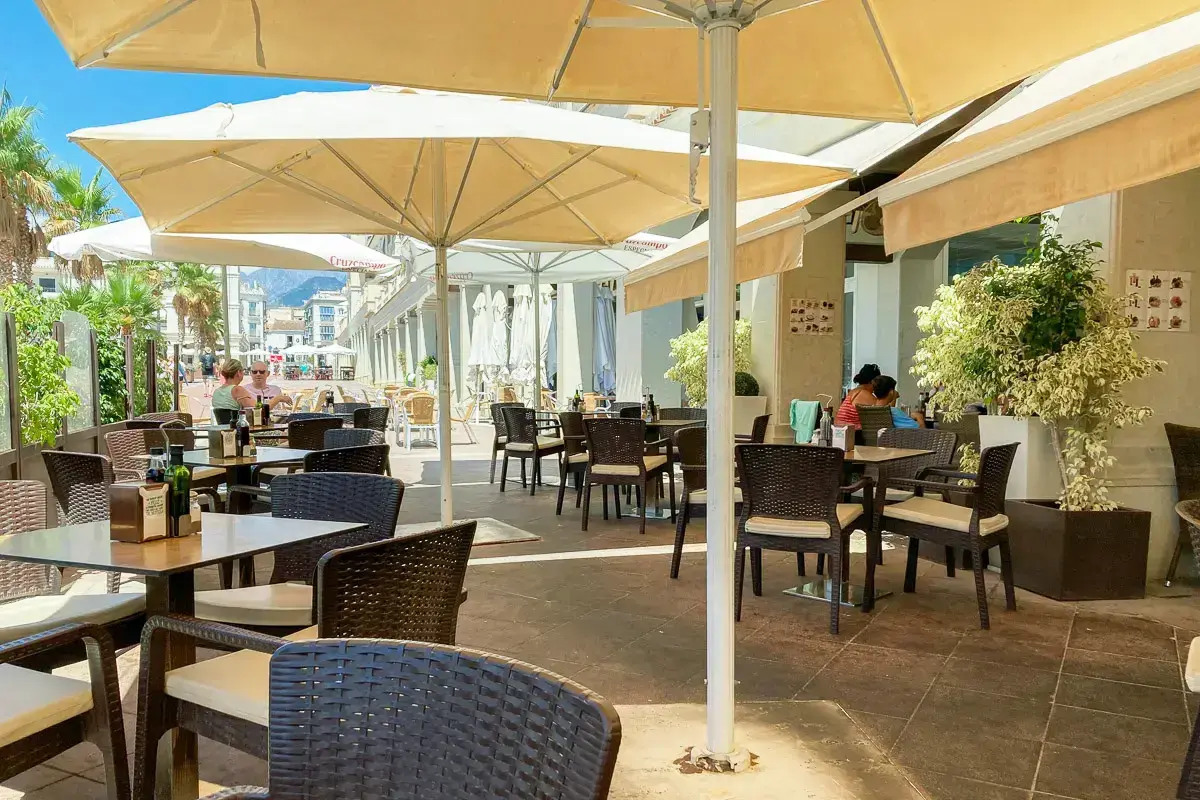 Terraza de la Cafetería Hermes con sillas de mimbre bajo grandes sombrillas en un día soleado