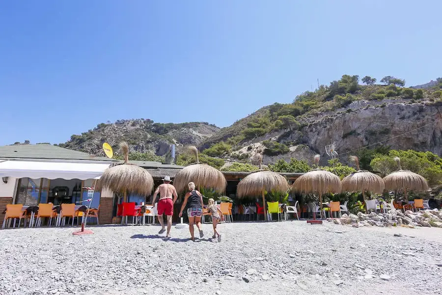 Chiringuito de la playa de Cantarriján con terraza y sombrillas de paja sobre la grava