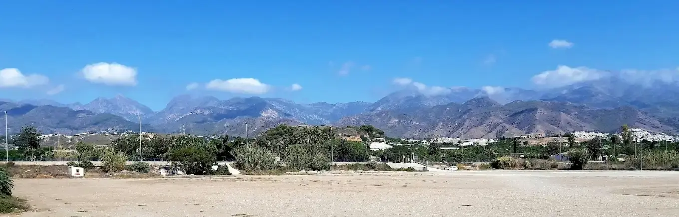 Gran explanada de aparcamiento de tierra con las sierras de Nerja de fondo