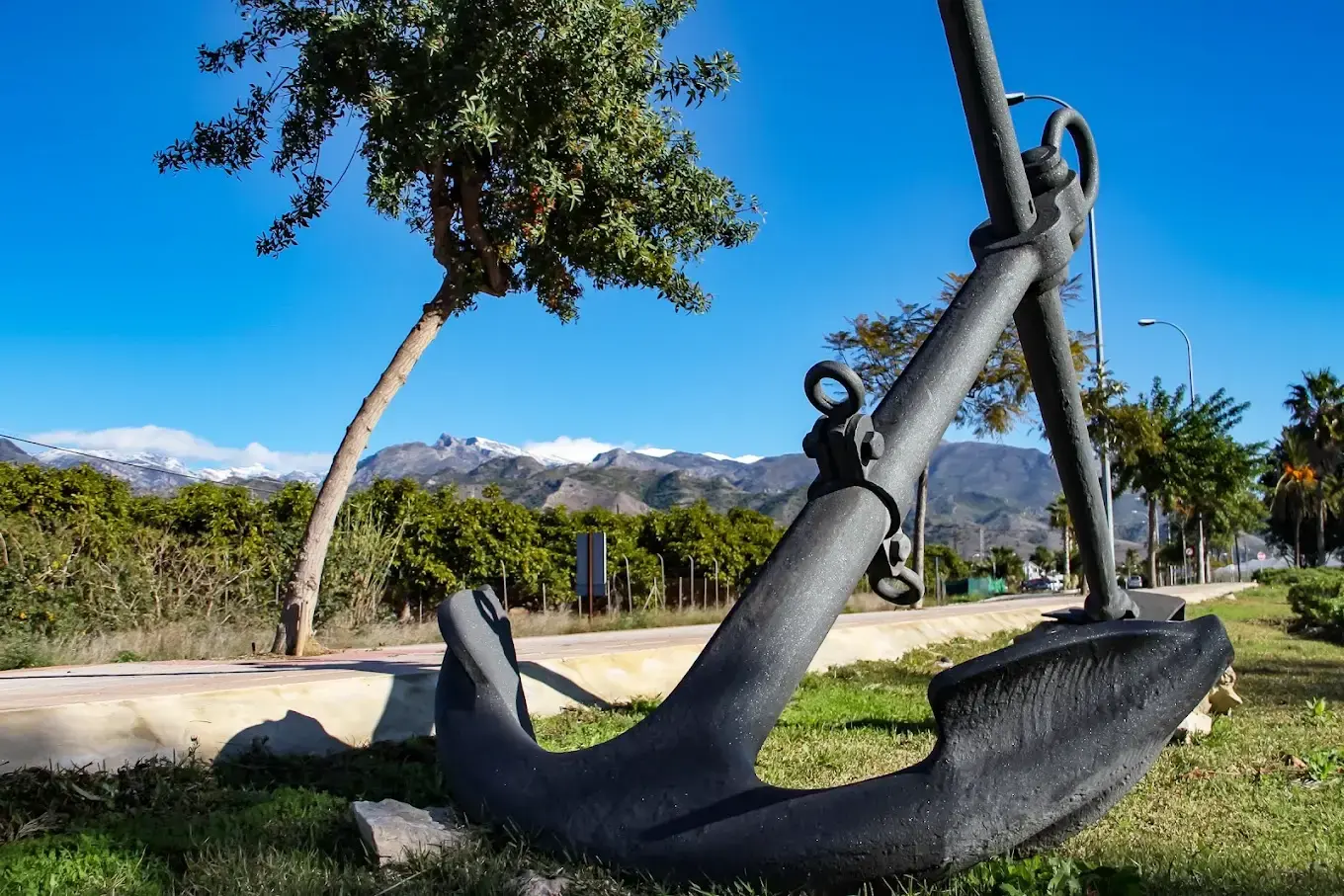Ancla de hierro en un jardín junto a la carretera, con las sierras nevadas al fondo