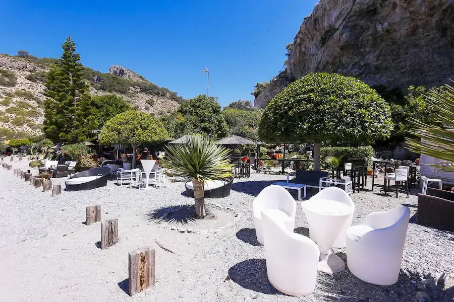 Terraza de un restaurante en la playa de Cantarriján, con sillones blancos y árboles