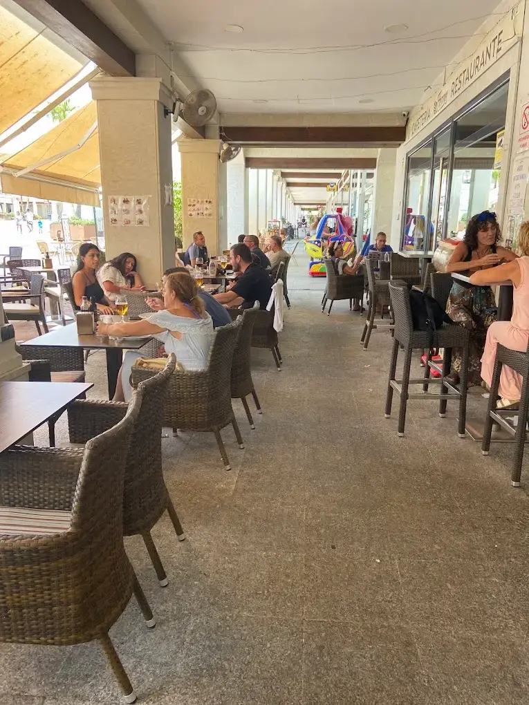 Clientes tomando algo bajo los soportales, con mesas altas y sillas de mimbre