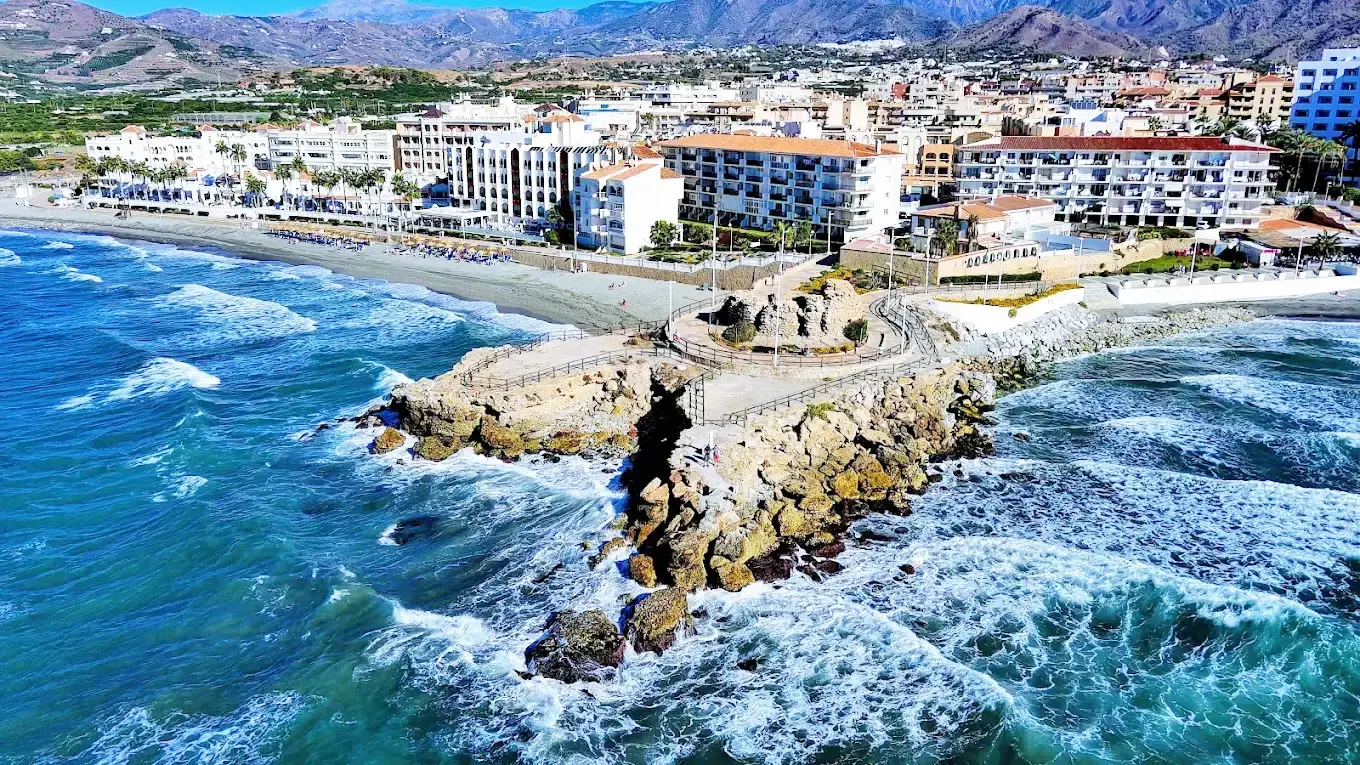 Olas rompiendo contra el espigón de La Torrecilla, con hoteles y playa detrás