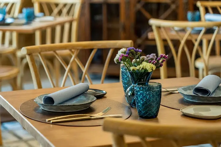 Mesa preparada con platos grises, servilletas, vasos azules y un jarrón con flores secas