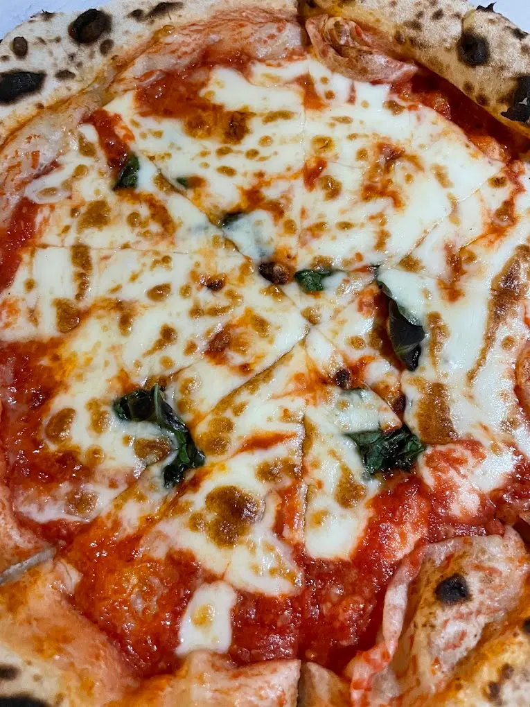Primer plano de una pizza margarita cortada con mozzarella fundida y albahaca
