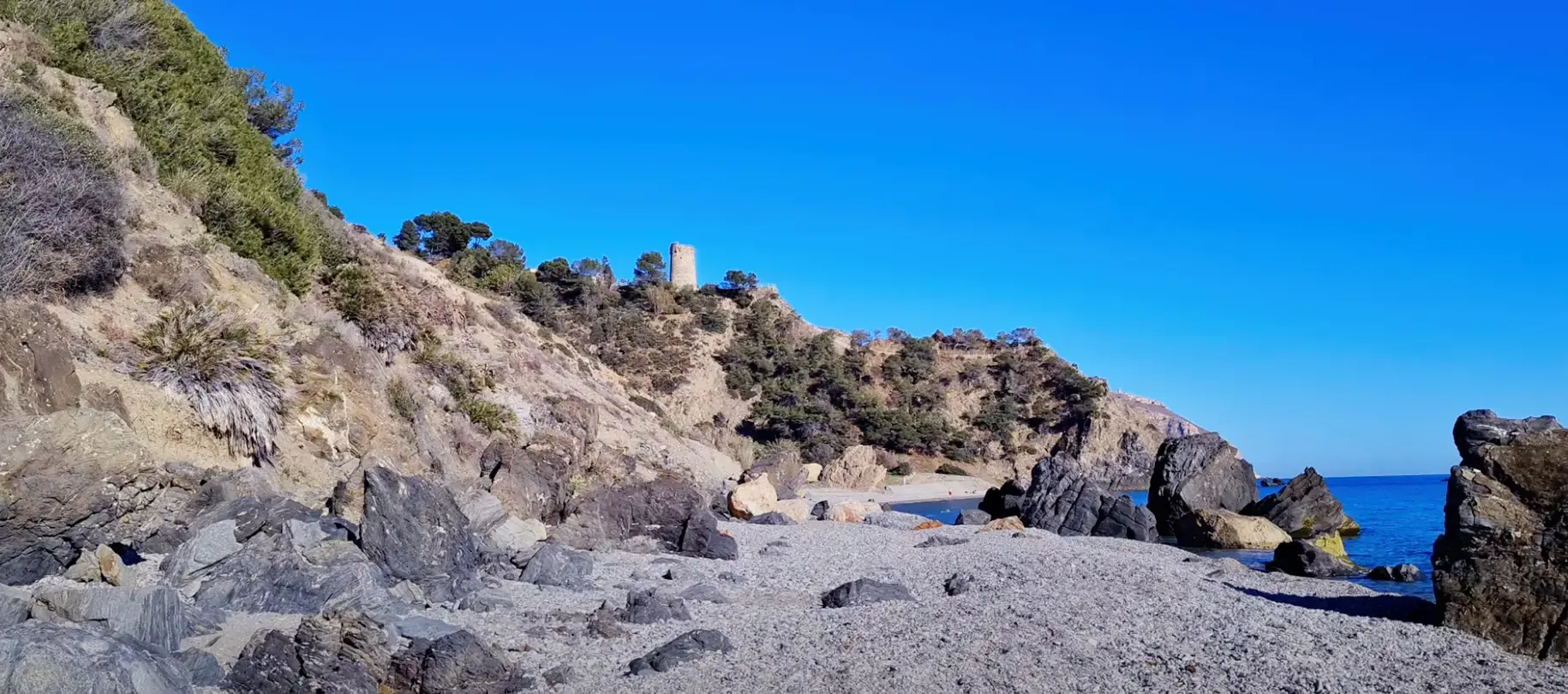 Rocas en la orilla de las Alberquillas, con una torre vigía en lo alto del cerro