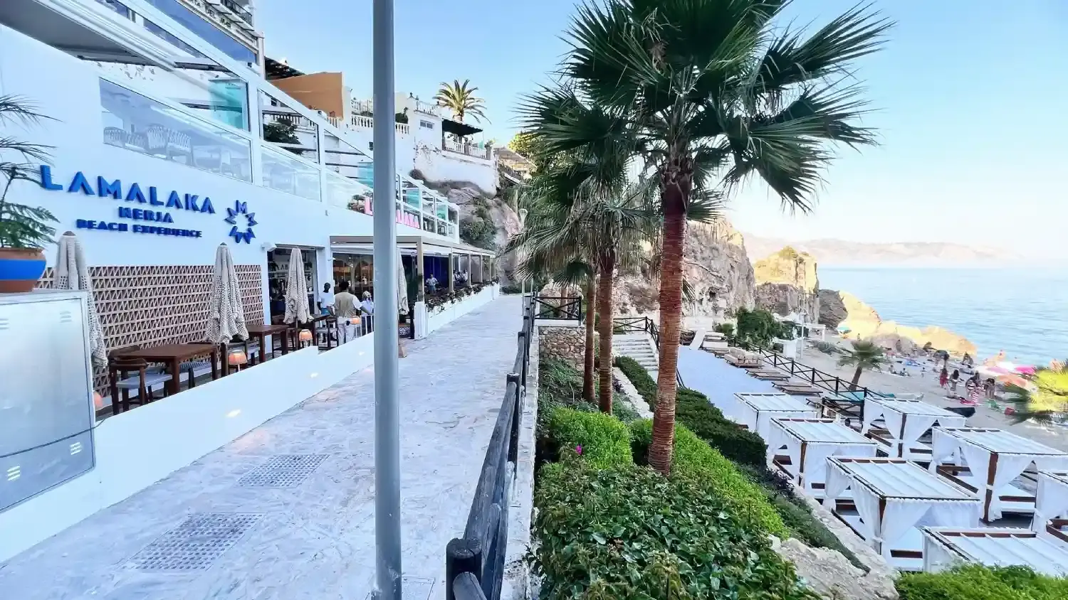 Paseo junto a La Malaka con mesas en la terraza, palmeras y vistas al mar