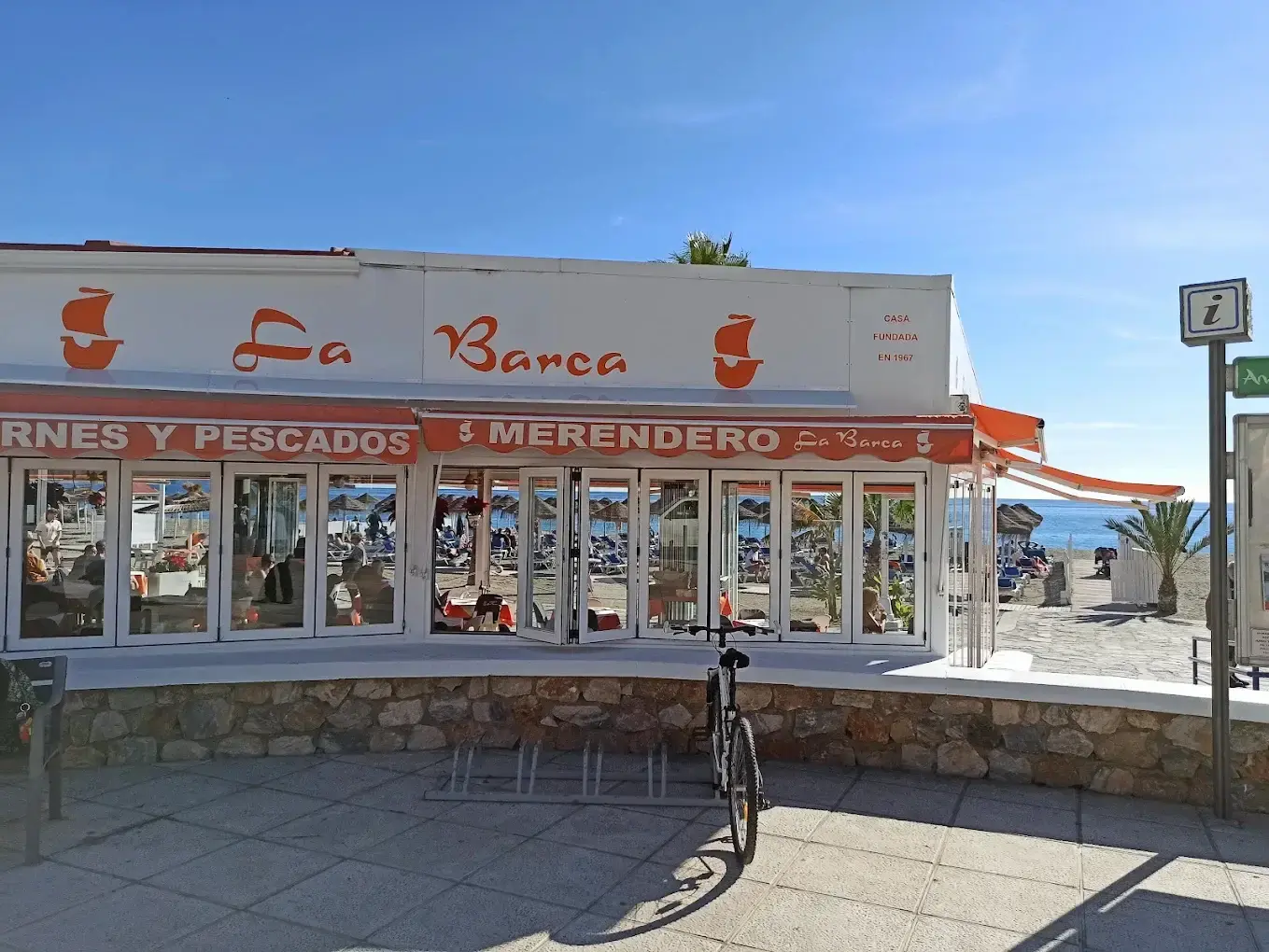 Fachada blanca del Merendero La Barca con cristaleras y la playa al fondo