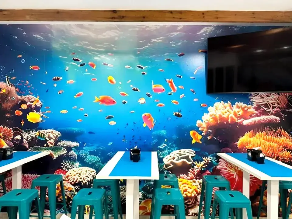 Mural de fondo marino con peces de colores sobre mesas blancas y taburetes turquesa