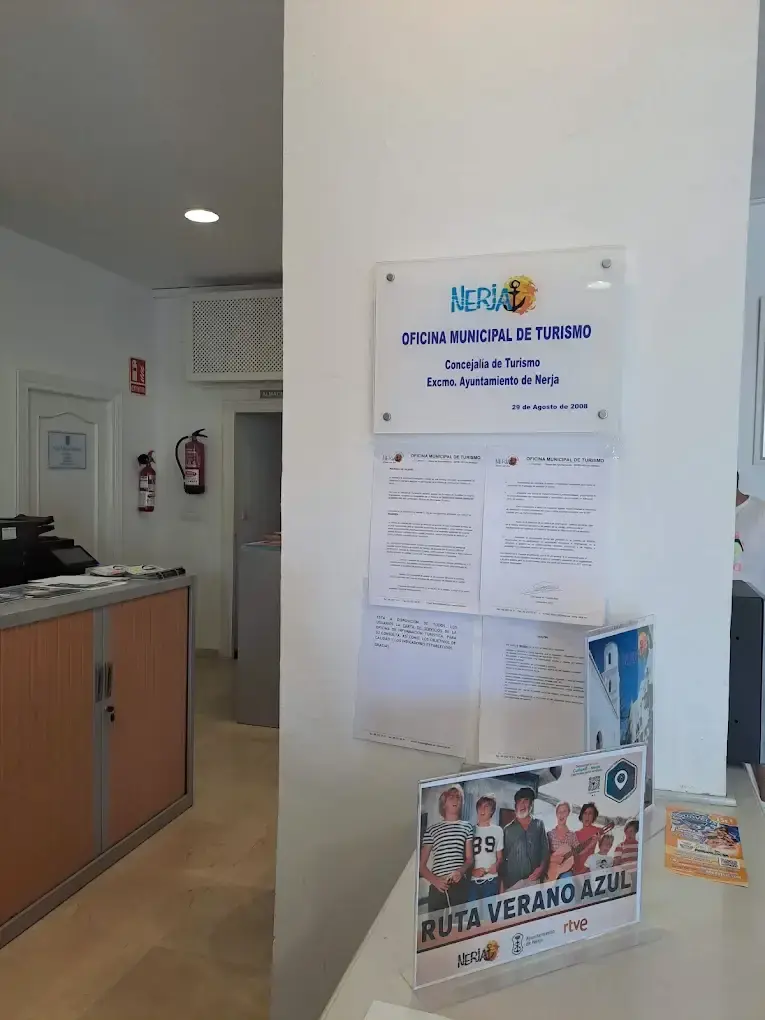 Placa de la Oficina Municipal de Turismo junto al mostrador, con un folleto de la Ruta Verano Azul
