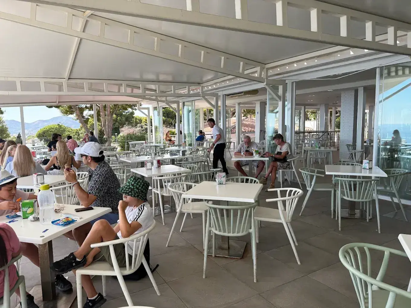 Terraza cubierta con comensales, sillas blancas y la sierra al fondo