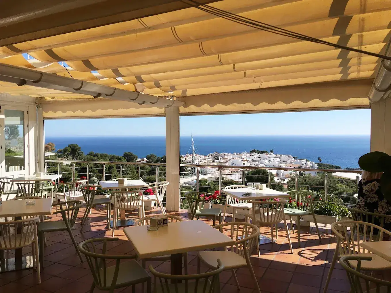 Terraza con toldo y mesas frente al pueblo blanco de Maro y el mar
