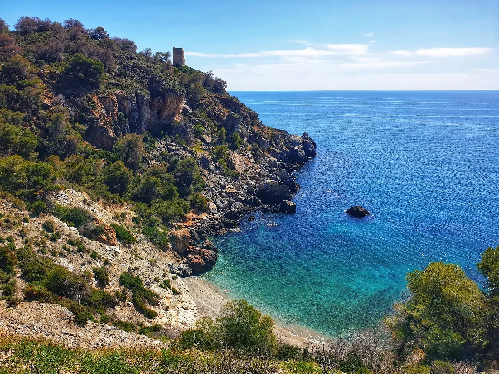 Cala de aguas turquesa bajo una torre vigía en los Acantilados de Maro-Cerro Gordo