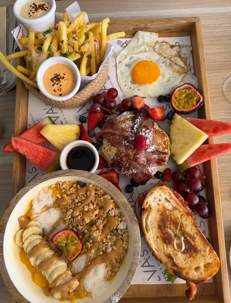 Bandeja de brunch con huevo frito, tortitas con beicon, fruta, patatas fritas y bol de granola
