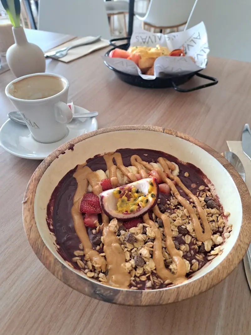 Bol de açaí con granola, plátano, fresas, maracuyá y crema de cacahuete junto a un café