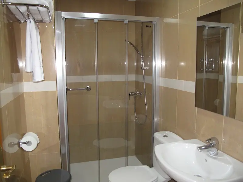 Baño con ducha de mampara, lavabo, inodoro y paredes alicatadas en tono beige
