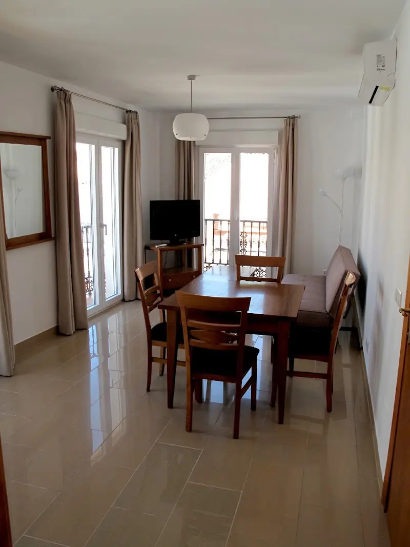 Salón comedor con mesa de madera, sillas, televisor y dos puertas a balcones