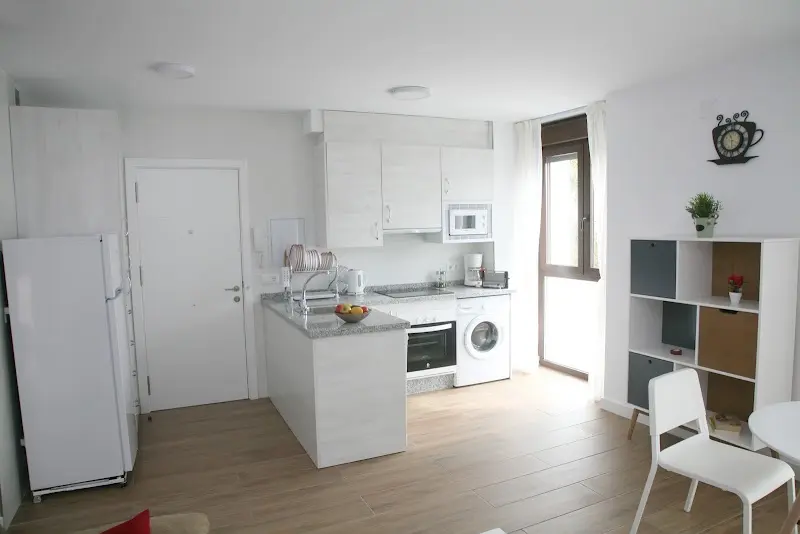 Cocina abierta con barra, horno, lavadora y nevera junto al salón del apartamento
