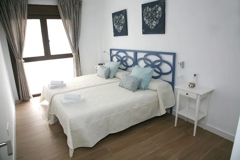 Dormitorio con dos camas, cabecero azul de forja y toallas preparadas sobre la colcha