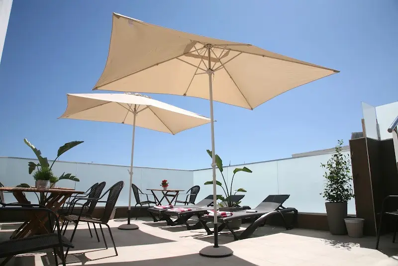 Terraza en la azotea con sombrillas, mesas, sillas, tumbonas y plantas