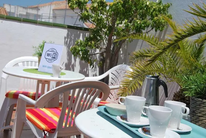 Mesa de terraza con tazas y cafetera, sillas con cojines de rayas y cartel de wifi