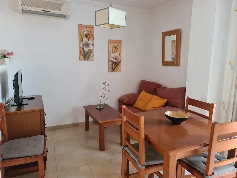 Salón con sofá rojo de cojines amarillos, mesa baja y mesa de comedor de madera