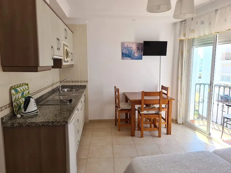 Estudio con cocina, mesa de comedor, televisión y puerta corredera a un balcón