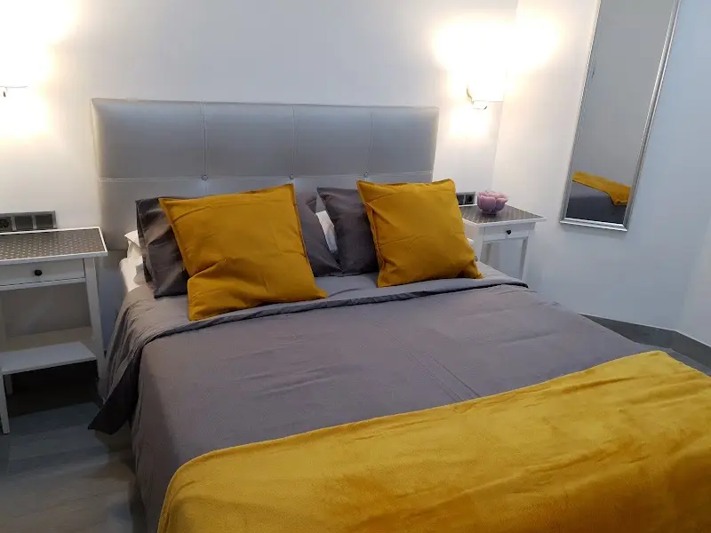 Dormitorio con cama de matrimonio, cabecero gris tapizado y cojines y manta mostaza