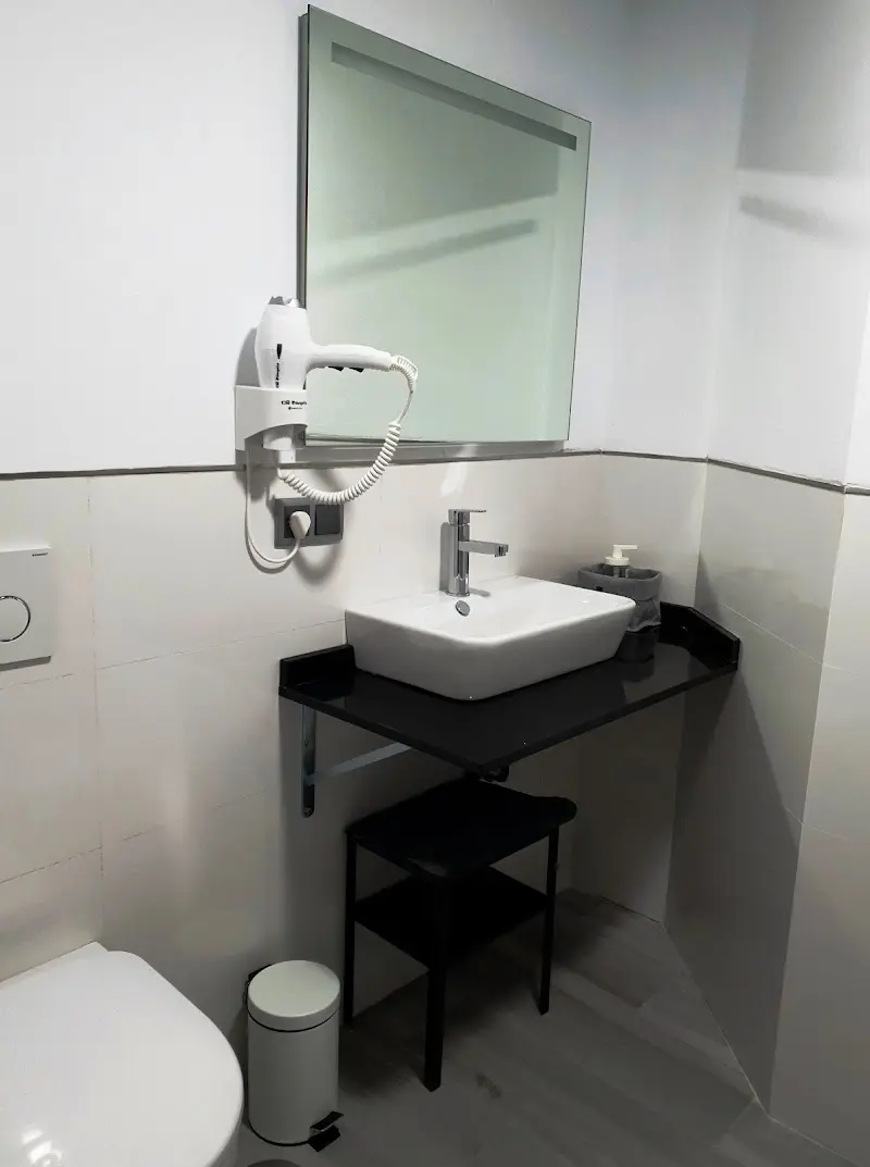 Baño con lavabo sobre encimera negra, espejo, secador de pelo e inodoro suspendido