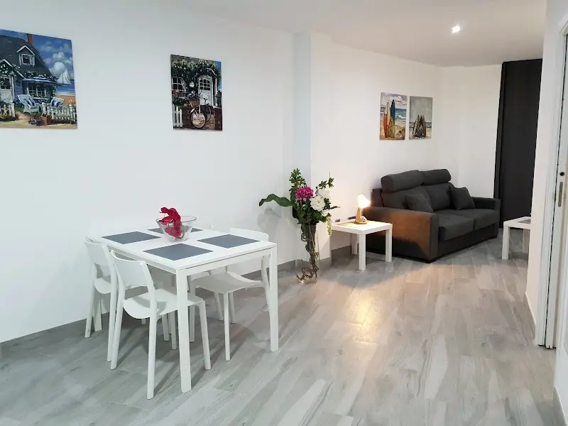 Salón comedor con mesa blanca para cuatro, sofá gris y cuadros marineros