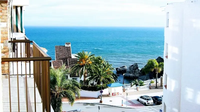 Vista desde un balcón a la calle, las palmeras, las rocas de la costa y el mar