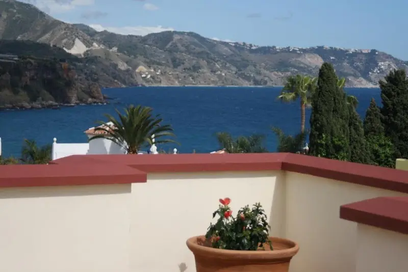 Terraza con maceta de flores y vistas al mar y a los acantilados de la costa hacia Maro