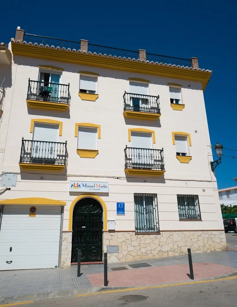 Fachada blanca y amarilla de Apartamentos Manuel Martín con balcones de forja y puerta en arco