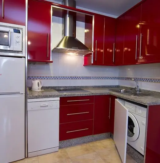 Cocina con muebles rojos brillantes, campana de acero, lavavajillas y lavadora