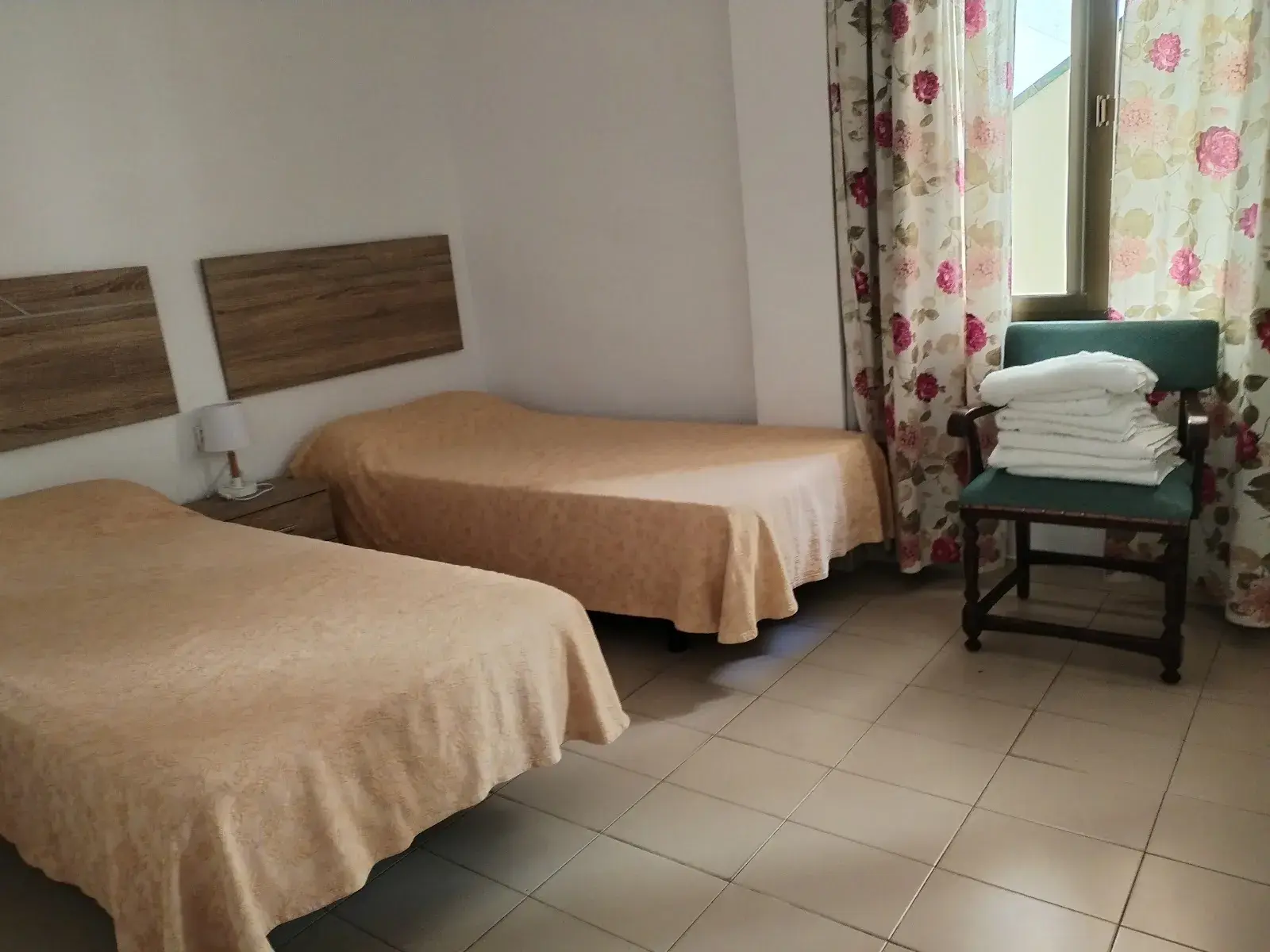 Dormitorio con dos camas de colcha naranja, cabeceros de madera y sillón