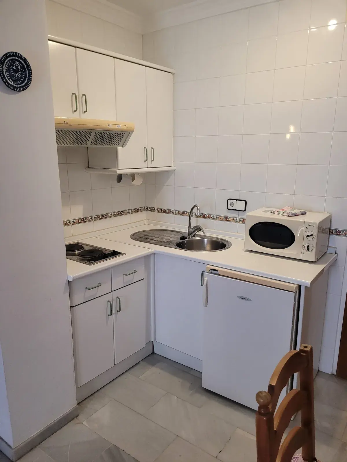 Cocina pequeña blanca con placa, fregadero, microondas y nevera
