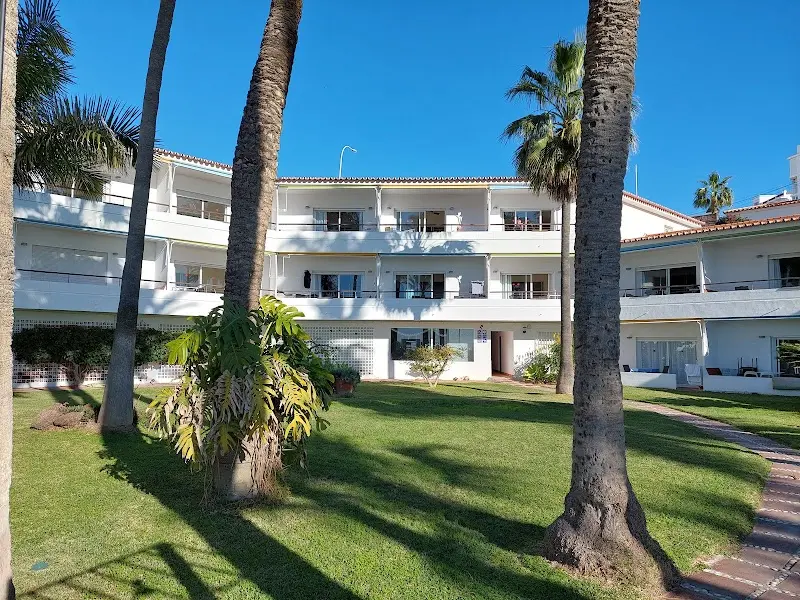 Bloque de los Apartamentos Playa Torrecilla con terrazas, rodeado de césped y palmeras