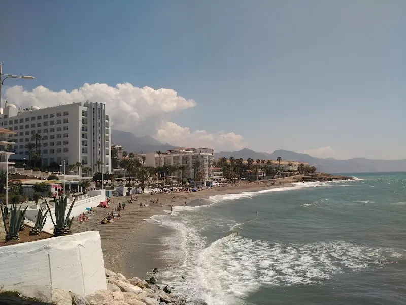 Playa de la Torrecilla con bañistas, olas en la orilla y edificios frente al mar
