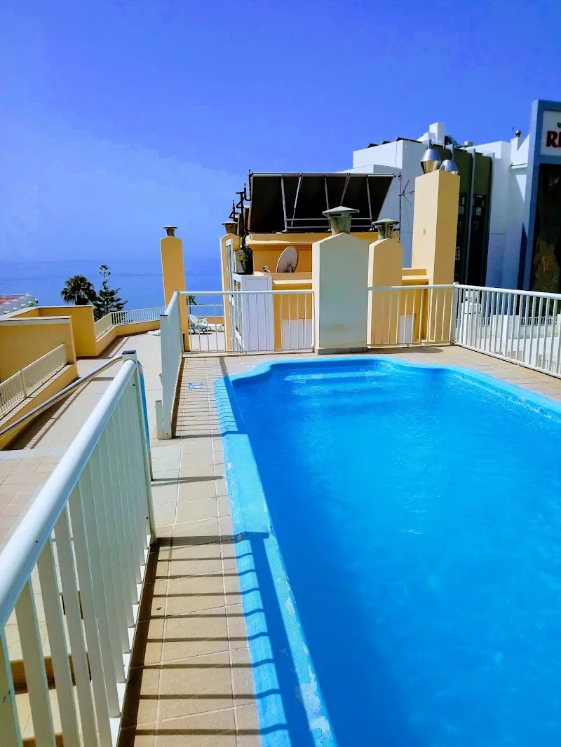 Piscina en la azotea con barandillas blancas y el mar asomando entre los edificios