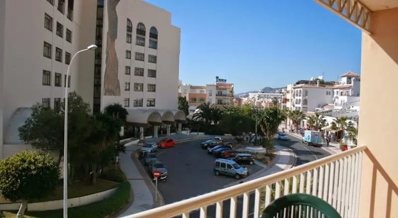 Calle con coches aparcados, farolas y edificios blancos vistos desde un balcón