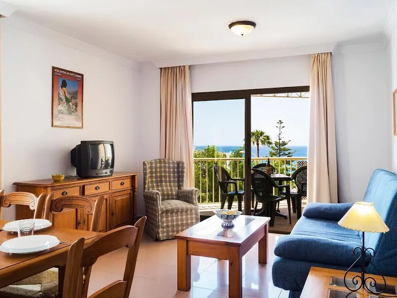 Salón con sofá azul, sillón, comedor de madera y terraza abierta con vistas al mar
