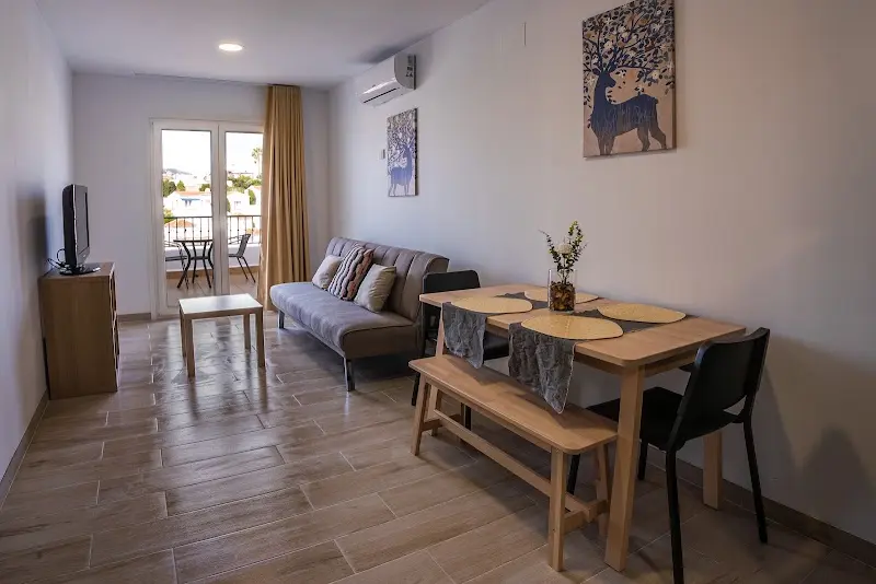 Salón con sofá gris, mesa de comedor con banco y puerta a una terraza con mesa