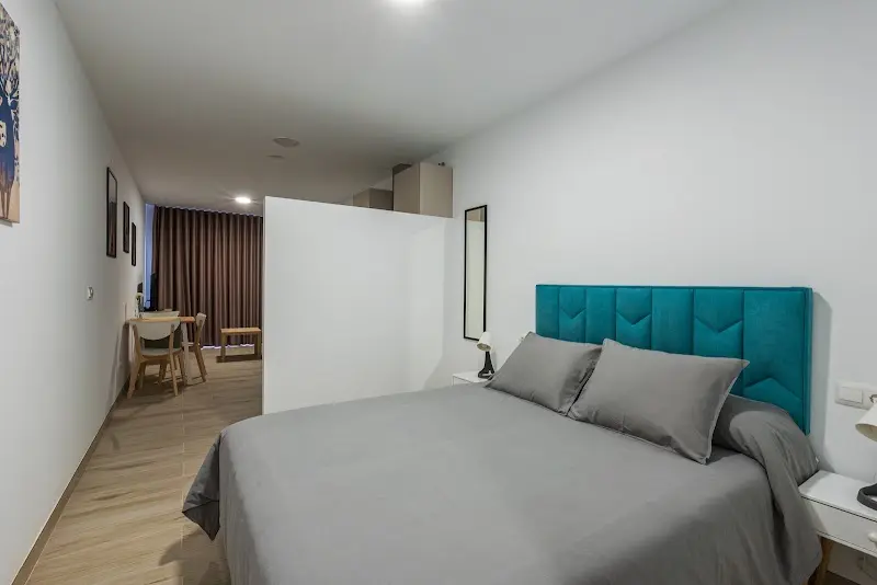 Dormitorio con cama de matrimonio, cabecero turquesa y el comedor al fondo