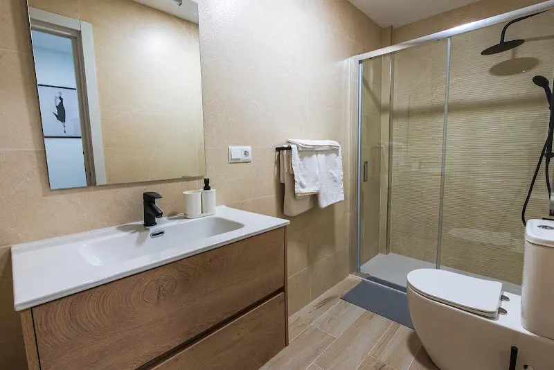 Baño moderno con lavabo sobre mueble de madera, espejo y ducha con mampara de cristal