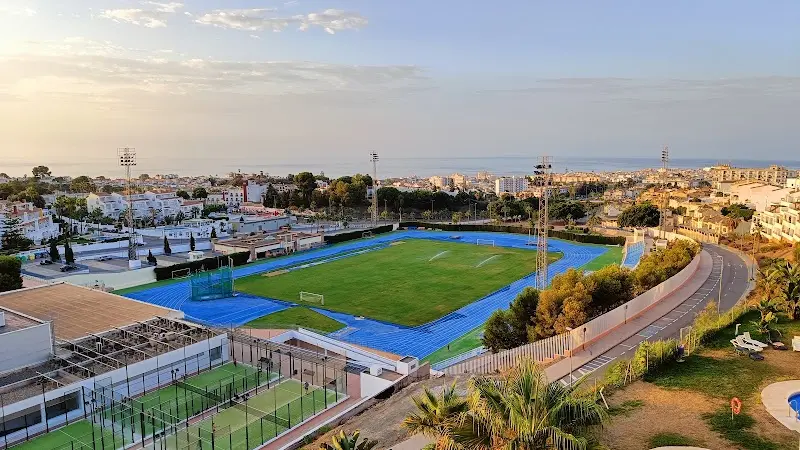 Vistas al estadio con pista de atletismo azul, pistas de pádel y el mar al fondo