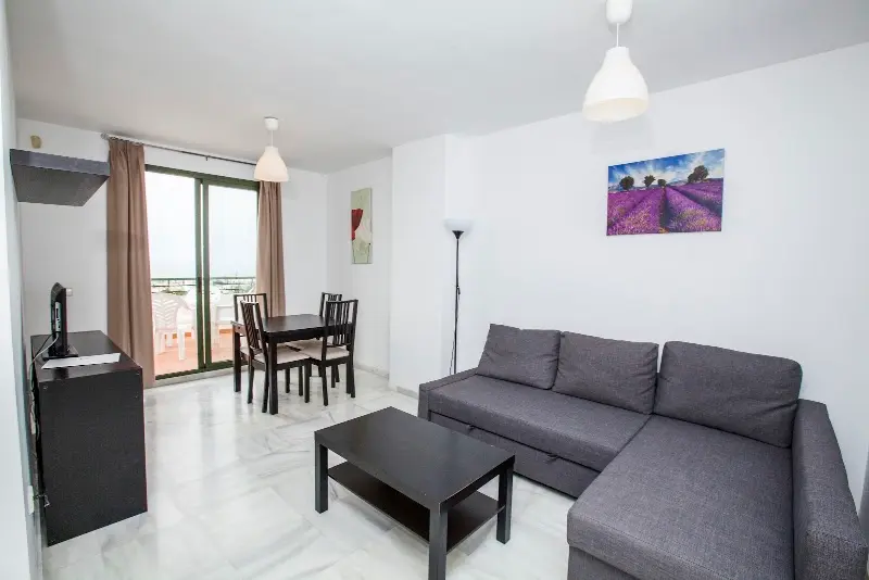 Salón con sofá chaise longue gris, mesa de comedor y salida a la terraza