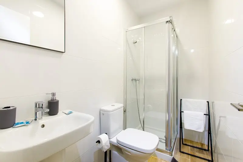 Baño blanco con plato de ducha con mampara, lavabo, inodoro y toallero